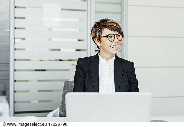 Smiling mature female entrepreneur looking away while sitting at desk in office