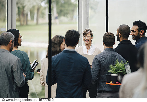 Smiling mature female entrepreneur talking to coworkers in office workshop