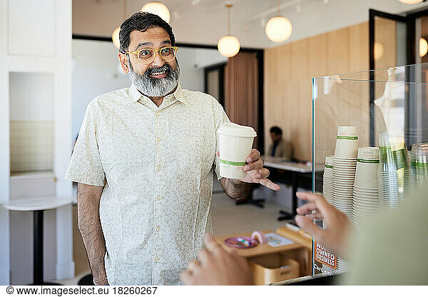 Smiling mature male customer receiving disposable coffee cup