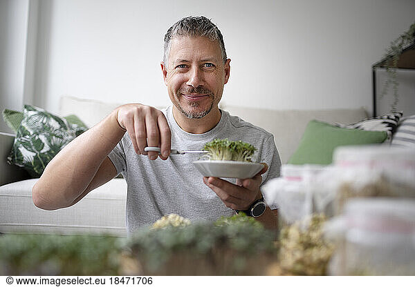 Smiling mature man cutting green herbs in living room