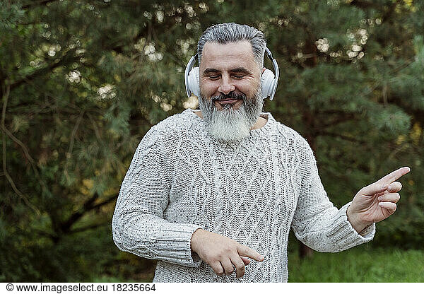 Smiling mature man listening to music through wireless headphones
