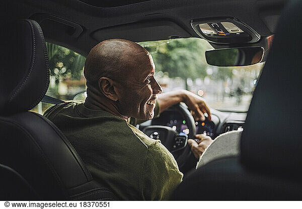 Smiling mature man looking away while sitting in car