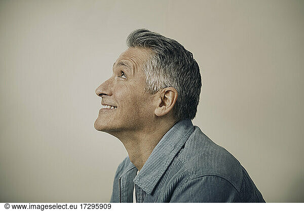 Smiling mature man looking up against beige background