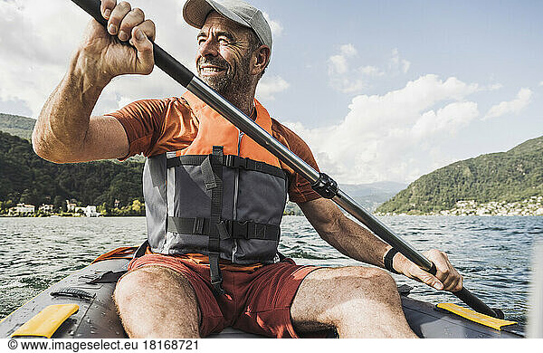 Smiling mature man rowing kayak boat on sunny day