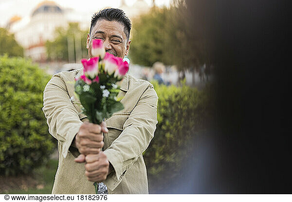Smiling mature man showing flowers in park on Valentine's day