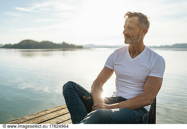 Smiling mature man sitting by lake on sunny day