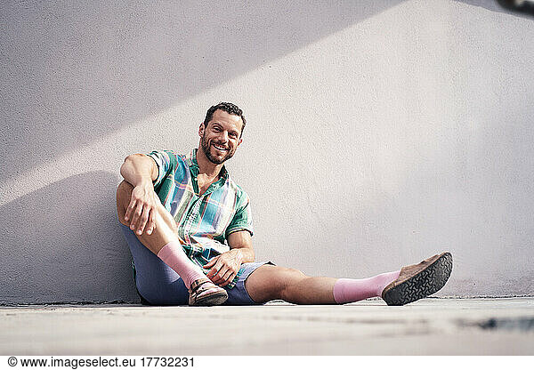 Smiling mature man sitting on floor near concrete wall