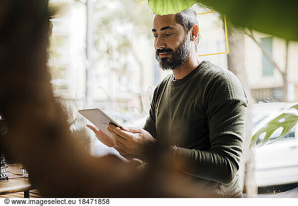 Smiling mature man using tablet PC in cafe
