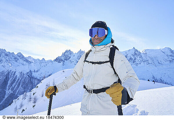 Smiling mature man wearing ski goggles standing in snow