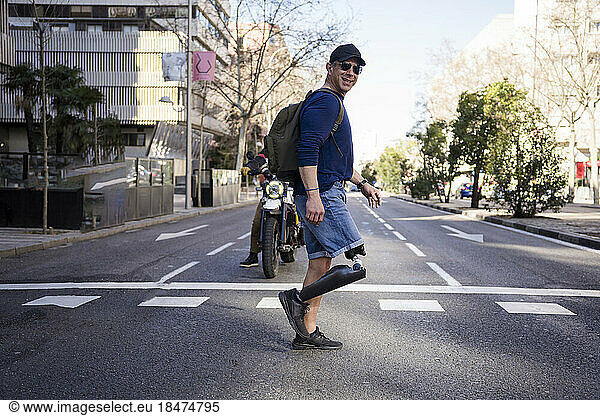 Smiling mature man with amputated leg crossing road in city