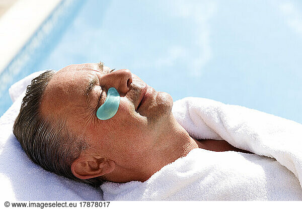Smiling mature man with collagen patch below eye at pool spa