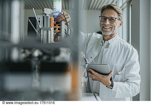 Smiling mature man with digital tablet inventing machinery in laboratory