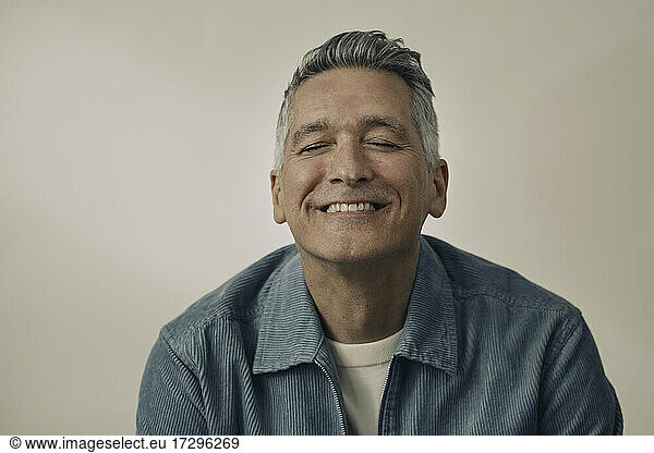 Smiling mature man with eyes closed against beige background