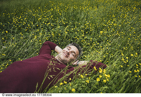 Smiling mature man with hands behind head lying on grass