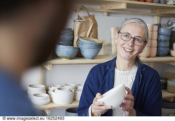 Smiling mature woman discussing with man over bowl in pottery class