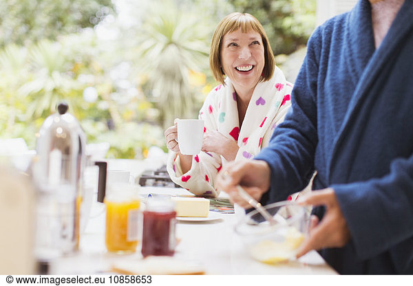 Smiling mature woman drinking coffee in bathrobe at breakfast