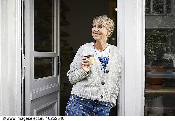 Smiling mature woman having coffee at entrance of art studio