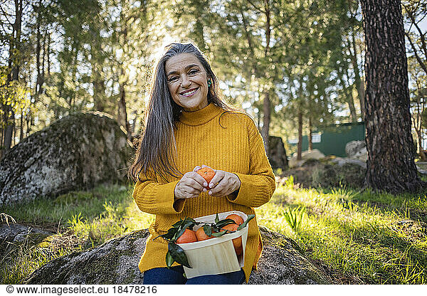 Smiling mature woman holding crate with tangerines