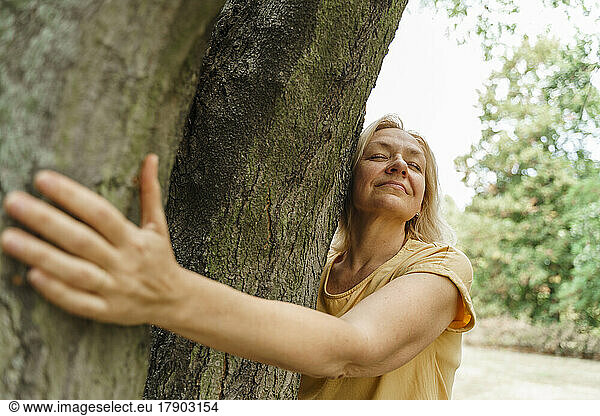 Smiling mature woman hugging tree at park