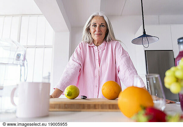 Smiling mature woman leaning on kitchen counter at home