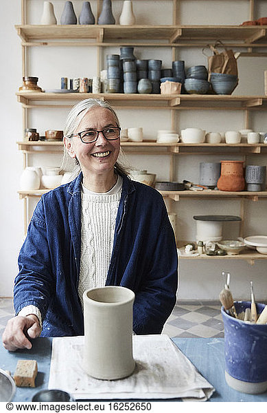 Smiling mature woman looking away while sitting at table in art class