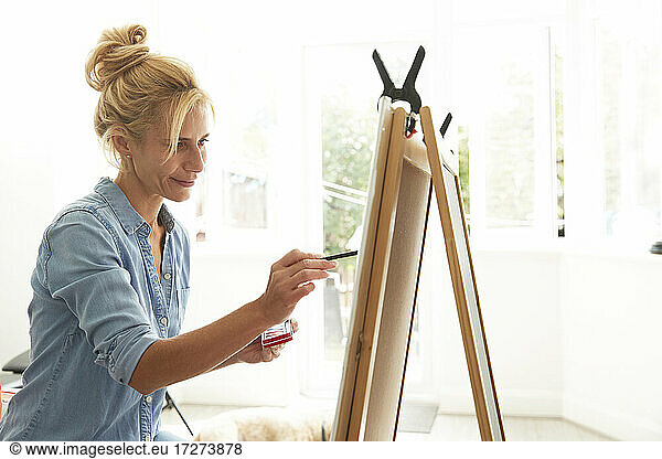 Smiling mature woman painting on paint board at home