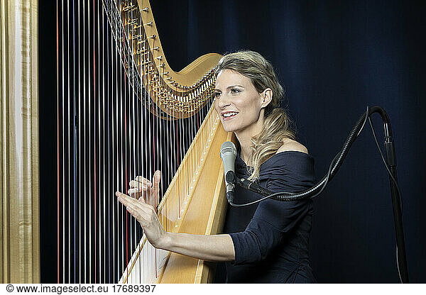 Smiling mature woman playing harp in front of black background