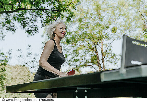 Smiling mature woman playing table tennis in park