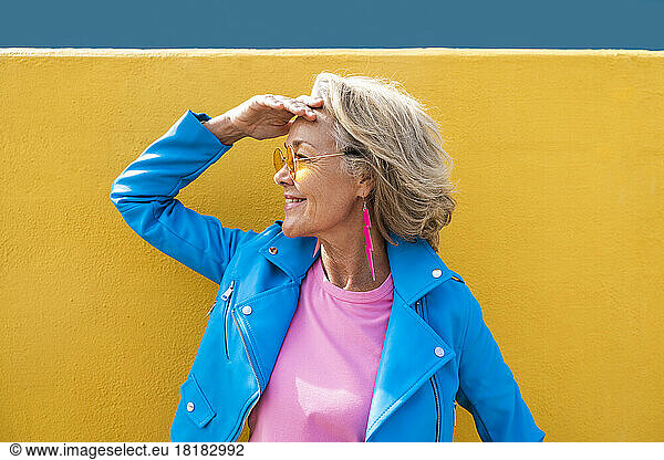 Smiling mature woman shielding eyes in front of wall