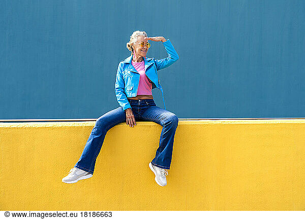 Smiling mature woman shielding eyes on yellow wall