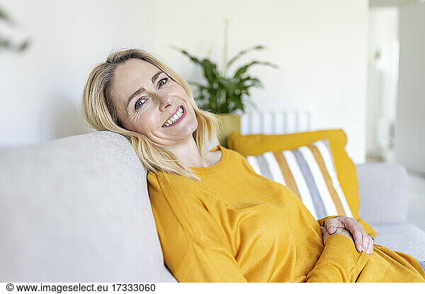 Smiling mature woman sitting on sofa at home