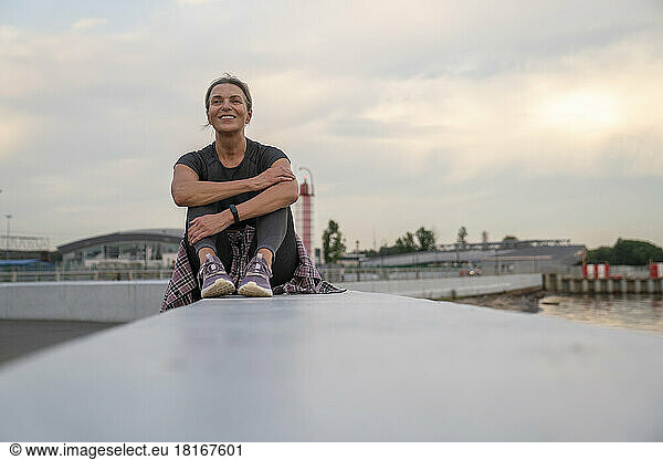 Smiling mature woman sitting on wall at sunset