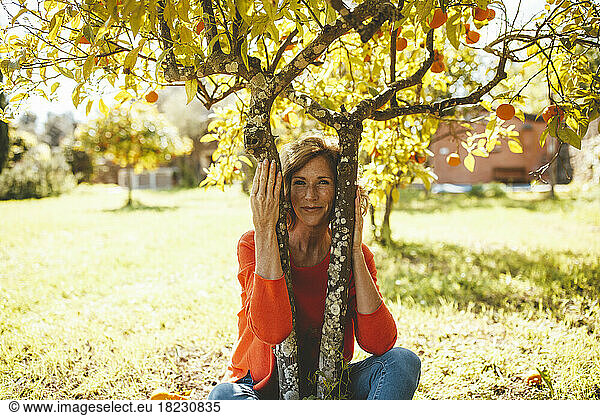 Smiling mature woman sitting under orange fruit tree