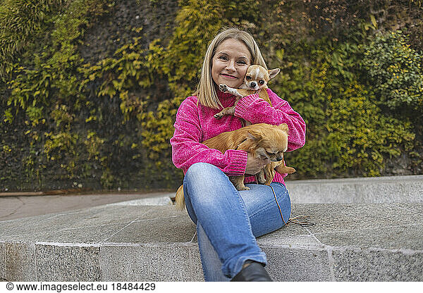 Smiling mature woman sitting with Chihuahua dogs on wall