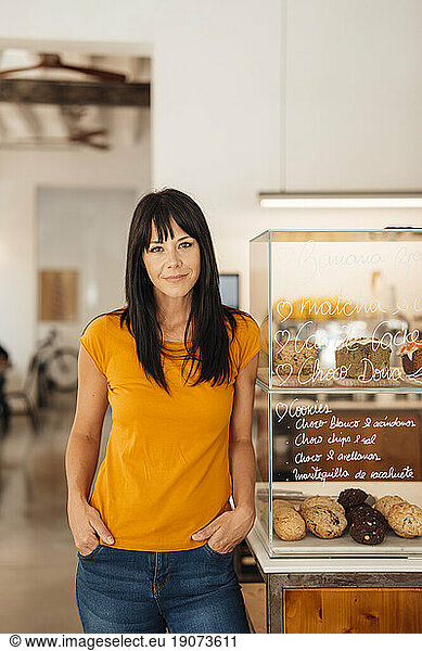 Smiling mature woman standing by retail display in cafe
