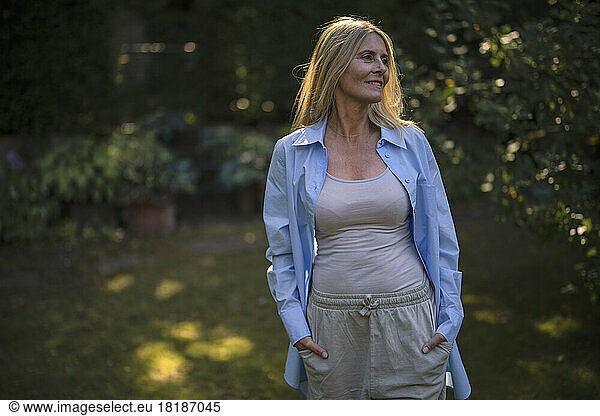 Smiling mature woman standing with hands in pockets at garden