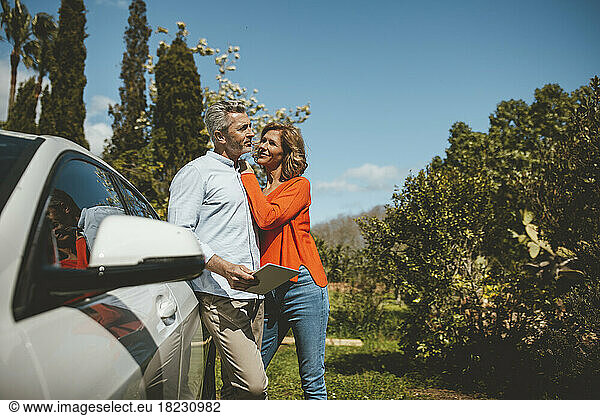 Smiling mature woman standing with man by car on sunny day
