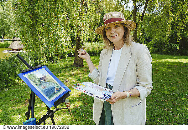 Smiling mature woman standing with watercolors in park