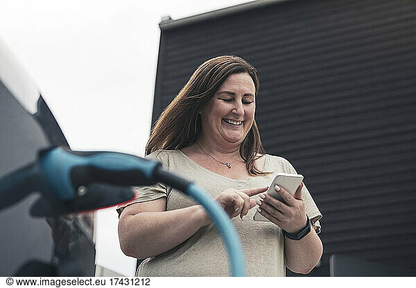 Smiling mature woman using smart phone at charging station