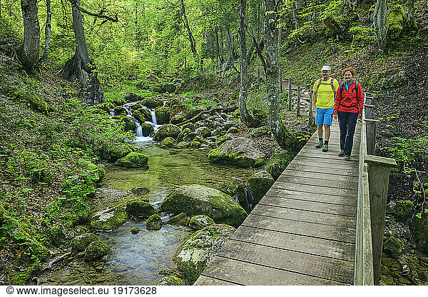 Smiling mature woman walking with man on wooden footbridge in forest