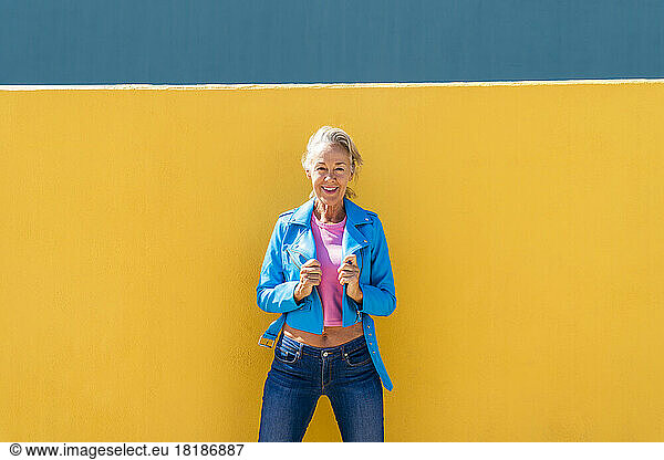 Smiling mature woman wearing blue leather jacket in front of colored wall