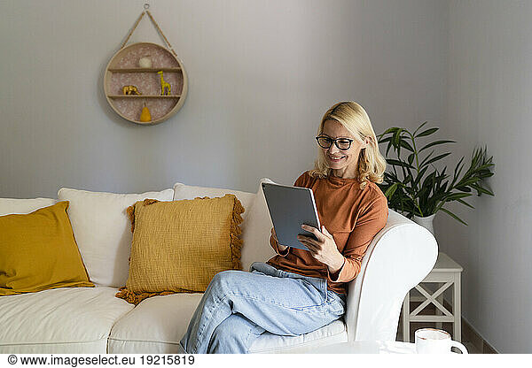 Smiling mature woman with eyeglasses using tablet PC in living room at home