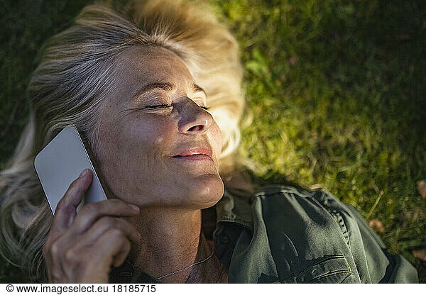 Smiling mature woman with eyes closed talking on mobile phone in garden