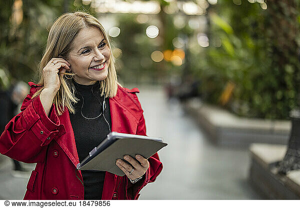Smiling mature woman with tablet PC standing on footpath