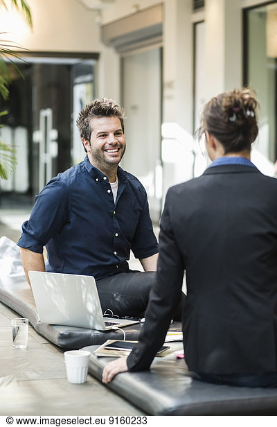 Smiling mid adult businessman discussing with female colleague at cafe