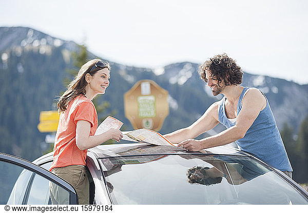 Smiling mid adult couple with map on car roof during road trip