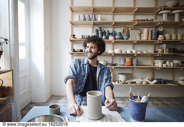 Smiling mid adult man looking away while sitting in pottery class