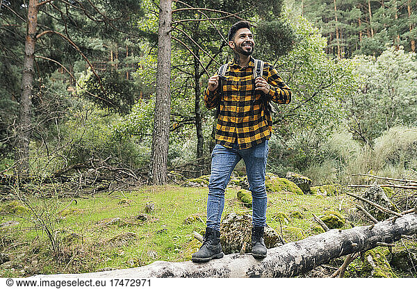 Smiling mid adult man standing on tree trunk in forest
