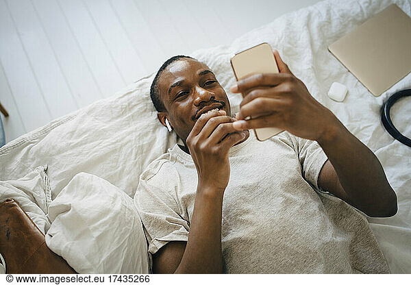 Smiling mid adult man using mobile phone while lying on bed