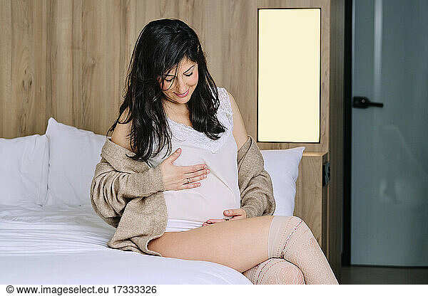 Smiling mid adult woman pregnant woman sitting on bed in bedroom
